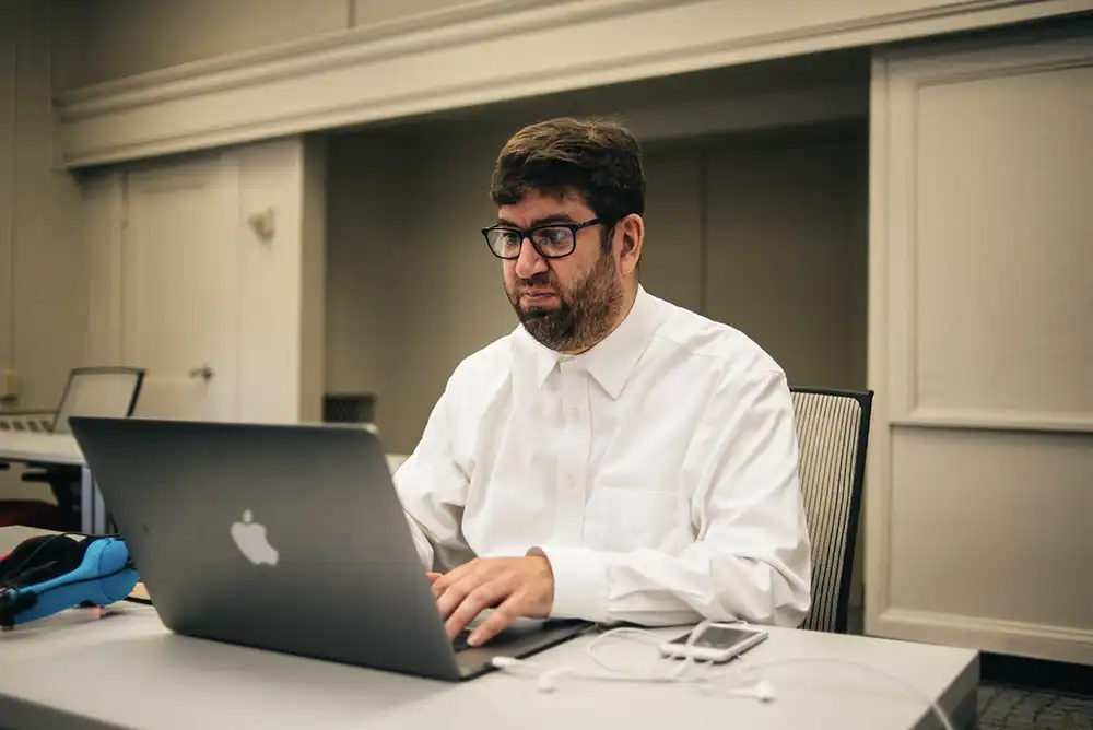 Man in formal business attire typing on laptop at desk.